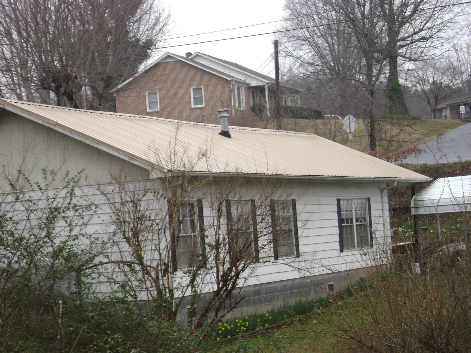 Tan metal roof on a white sided house set into a hillside — Commercial Roofing by Roofing Brothers in Durant